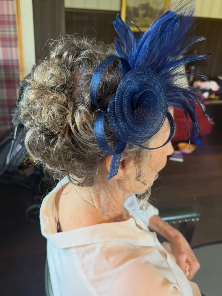 Curly updo with volume and a blue fascinator on an older woman