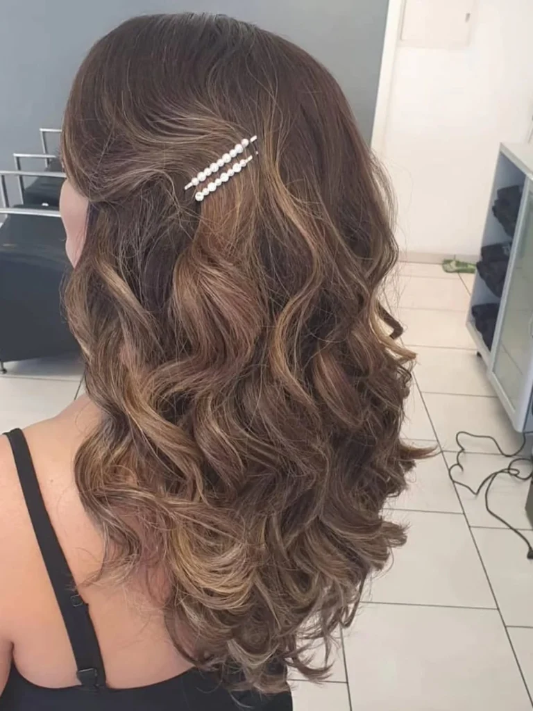 Half-up hairstyle with a pearl barrette on long wavy brown hair
